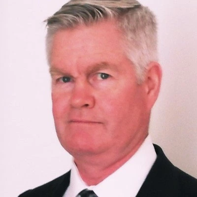 This image shows a professional headshot of a smiling man in formal attire, wearing a dark blazer over a light blue shirt. His approachable and friendly expression makes the portrait ideal for use in business-related settings such as LinkedIn profiles, corporate websites, and professional presentations. The neutral background ensures focus on the subject, highlighting his confident and positive demeanor, perfect for personal branding and networking.